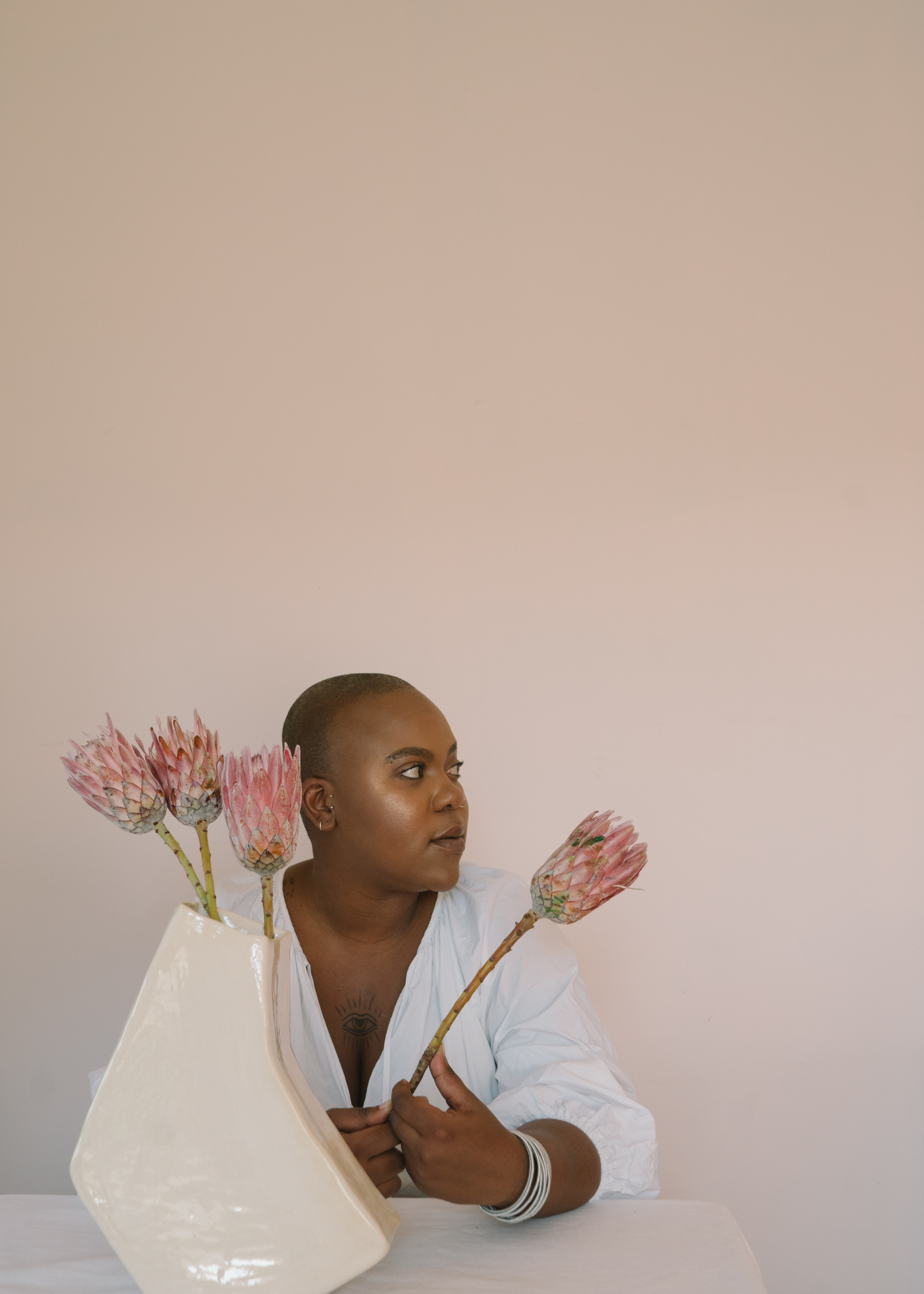 Bald Woman Sitting on a Table Holding a King Protea Flower